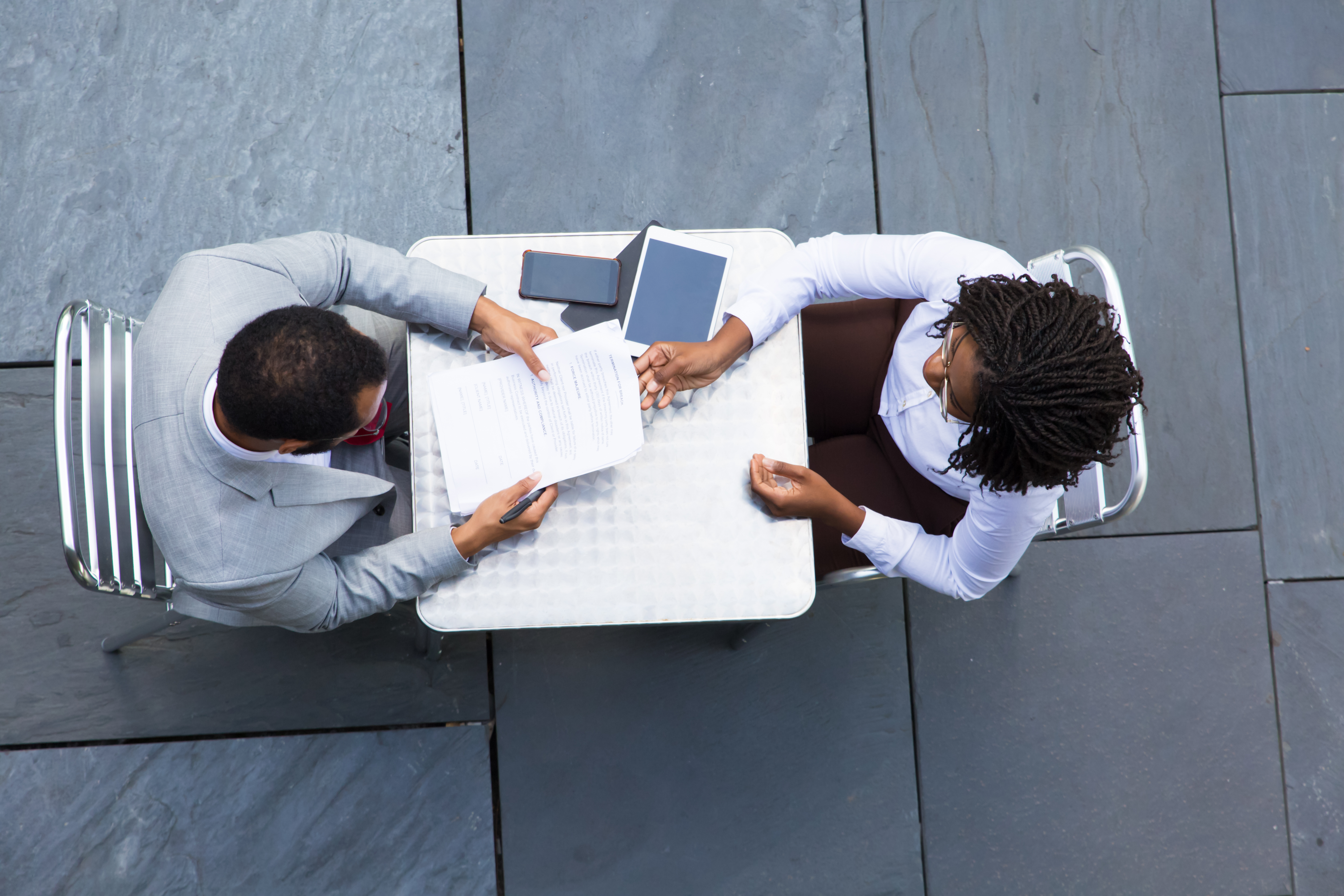 African American businesswoman passing documents to colleague. Two workers reading papers while sitting at table. Business meeting concept
